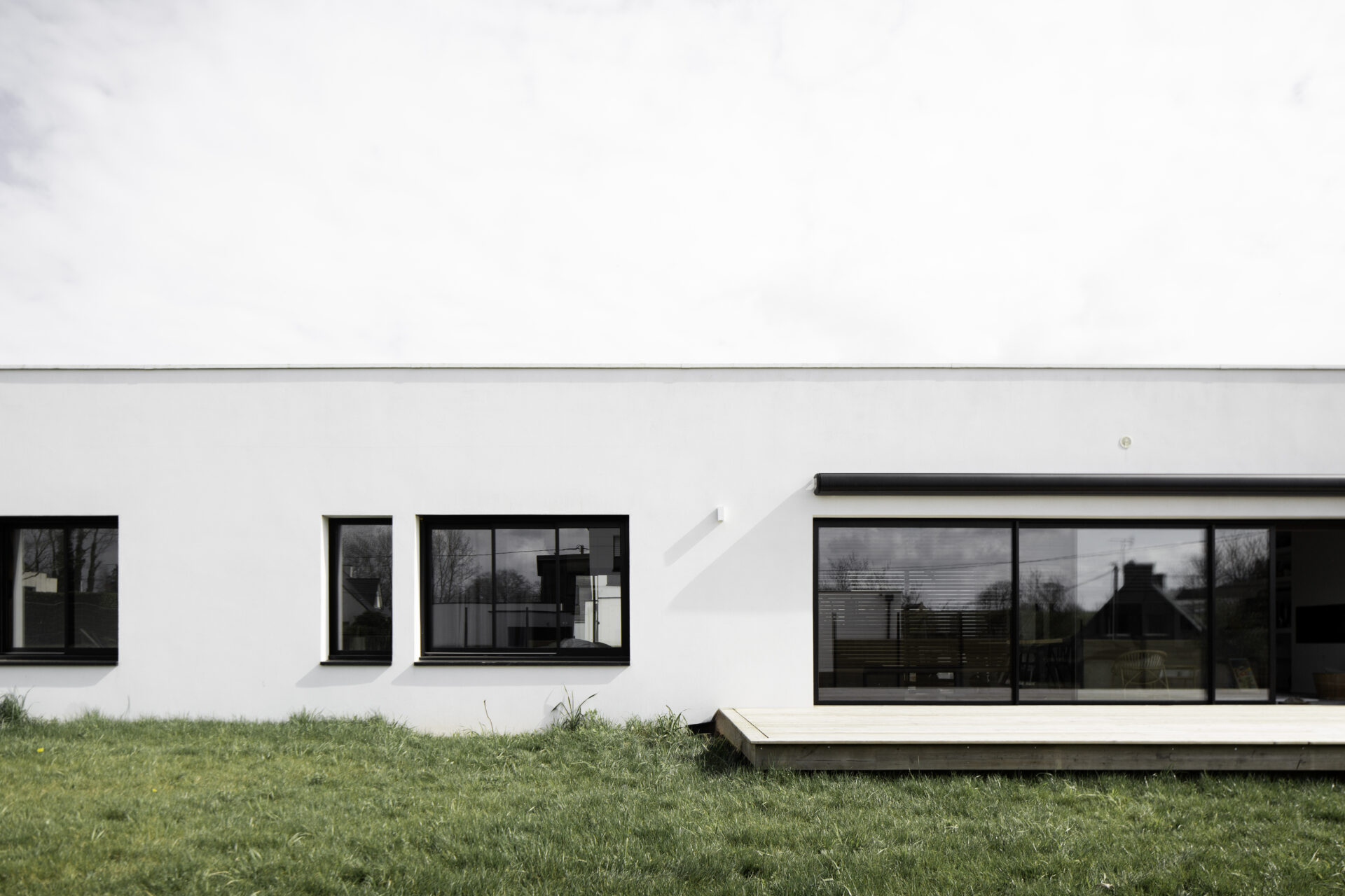 Création d'une maison individuelle de plein pied avec terrasse en bois. Menuiseries noires. Baies coulissantes.