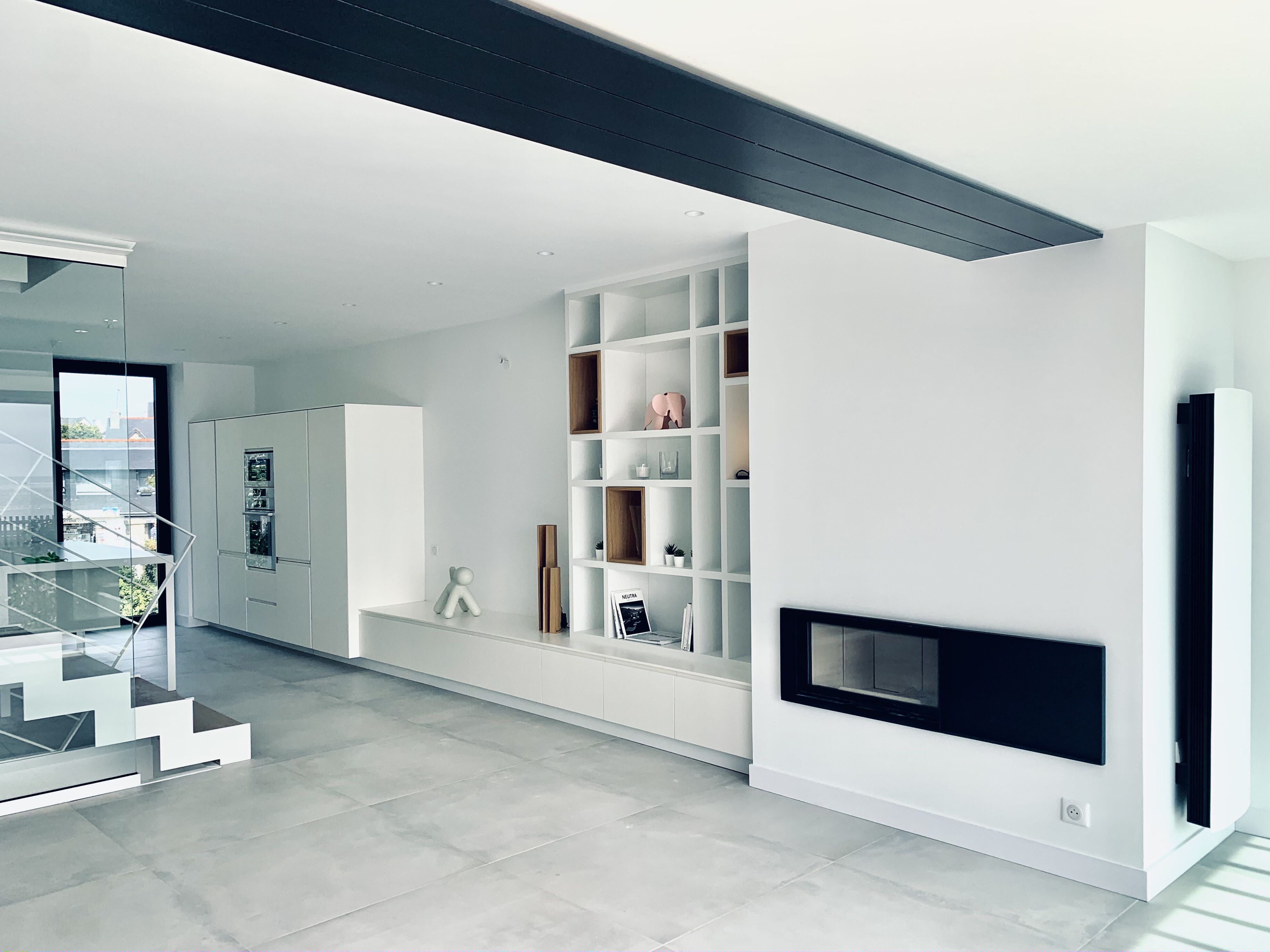 Agencement intérieur d'une maison. Rénovation avec carrelage gris et agencement d'une bibliothèque sur mesure. Niche bibliothèque sur mesure en médium laqué blanc avec rangements intégrés meuble sur mesure autour d'une cheminée.